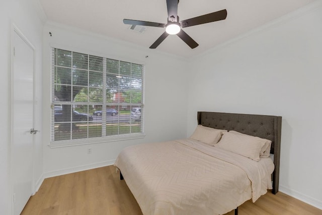 bedroom with light wood-type flooring, ornamental molding, baseboards, and a ceiling fan
