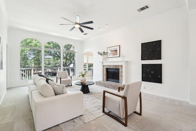 carpeted living room featuring a ceiling fan, a fireplace, baseboards, and arched walkways