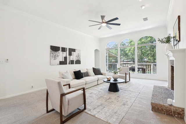 living room featuring carpet flooring, a ceiling fan, arched walkways, crown molding, and a fireplace
