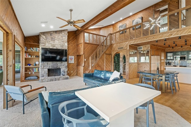 living area featuring wood walls, a ceiling fan, high vaulted ceiling, a fireplace, and stairway