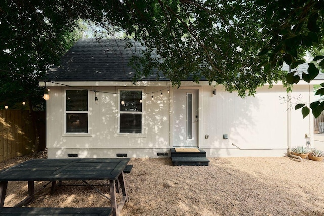 rear view of property with fence, crawl space, and a shingled roof