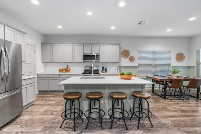 kitchen with stainless steel appliances, gray cabinets, a breakfast bar area, light wood-style floors, and recessed lighting