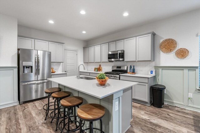 kitchen featuring stainless steel appliances, a sink, gray cabinets, wood finished floors, and recessed lighting