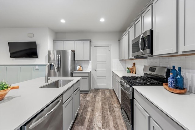 kitchen featuring appliances with stainless steel finishes, a sink, light countertops, light wood finished floors, and gray cabinetry