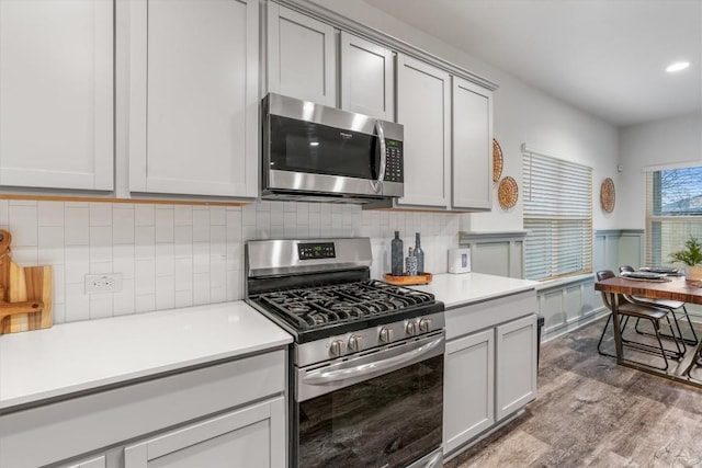 kitchen with stainless steel appliances, light countertops, wood finished floors, tasteful backsplash, and wainscoting