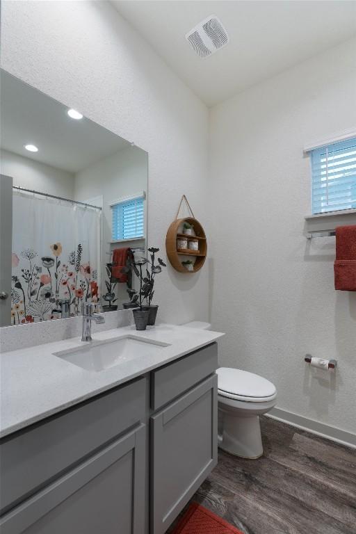 bathroom with wood finished floors, toilet, vanity, baseboards, and recessed lighting