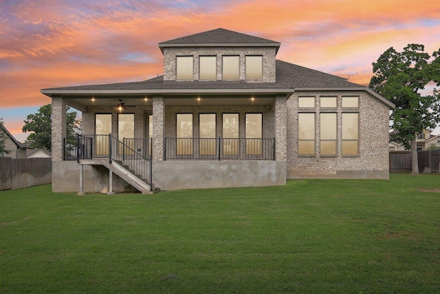 back of house at dusk with a shingled roof, ceiling fan, and stairway