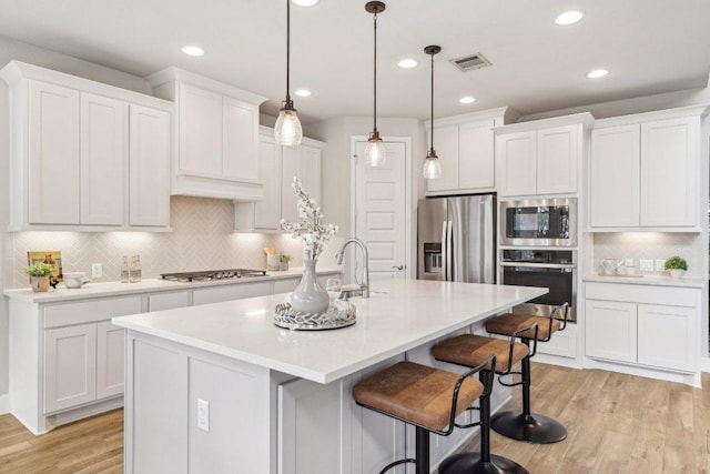 kitchen featuring appliances with stainless steel finishes, a sink, tasteful backsplash, light wood-style floors, and a kitchen breakfast bar