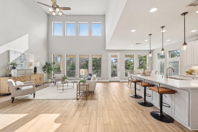 living room featuring light wood-style flooring, ceiling fan, recessed lighting, a high ceiling, and baseboards