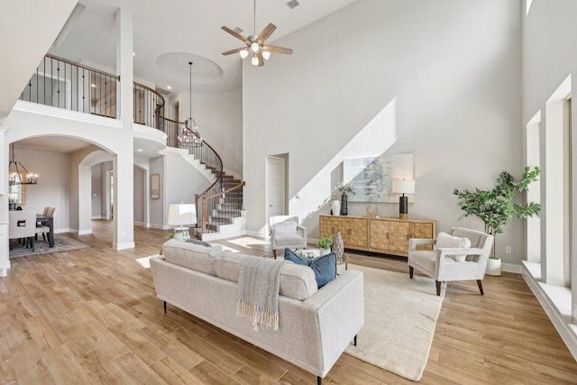 living room with a high ceiling, stairway, arched walkways, light wood-style floors, and a ceiling fan