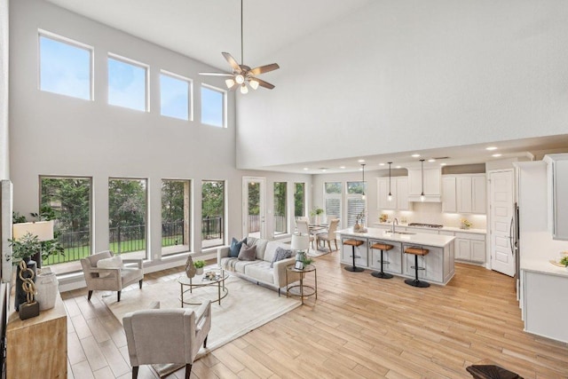 living room with a high ceiling, a ceiling fan, healthy amount of natural light, light wood-style floors, and recessed lighting