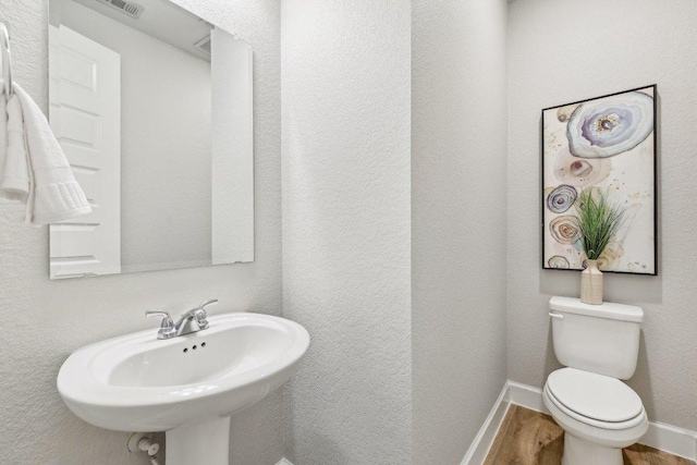 half bath with toilet, wood finished floors, baseboards, and a sink