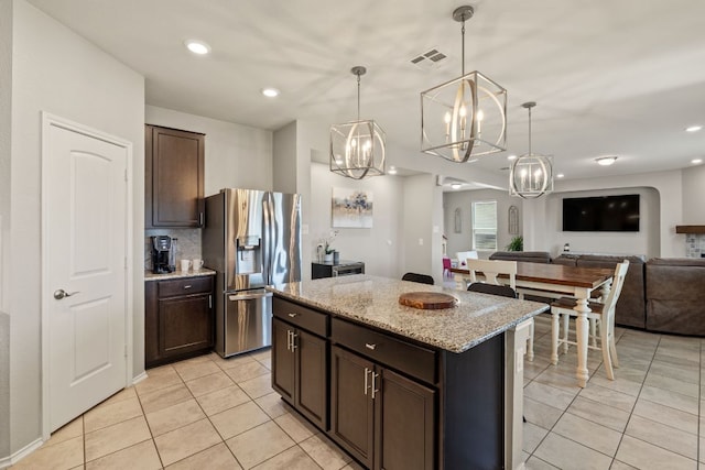kitchen with stainless steel fridge, light tile patterned floors, a chandelier, open floor plan, and dark brown cabinetry