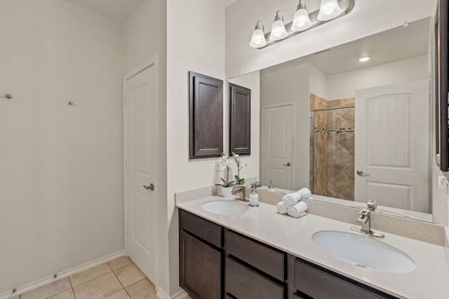 bathroom featuring a tile shower, tile patterned floors, double vanity, and baseboards