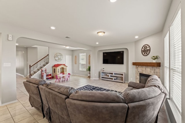 living area with light tile patterned floors, stairway, recessed lighting, a brick fireplace, and arched walkways