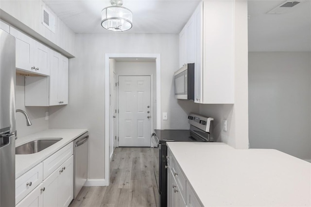 2201 Mission Hill Cir, Austin, TX 78741 - kitchen featuring appliances with stainless steel finishes, a sink, white cabinetry, light wood finished floors, and light countertops