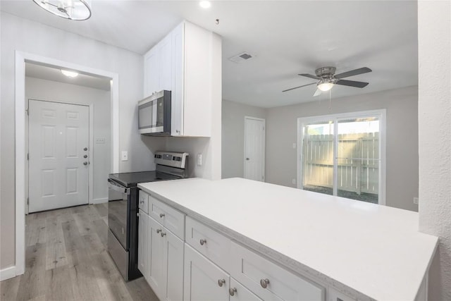 2201 Mission Hill Cir, Austin, TX 78741 - kitchen featuring stainless steel appliances, a peninsula, light wood-style floors, white cabinets, and a ceiling fan