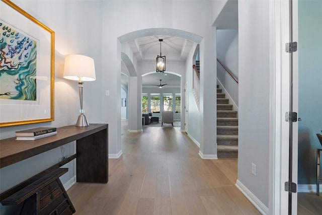 foyer featuring arched walkways, light wood-style floors, stairs, and baseboards