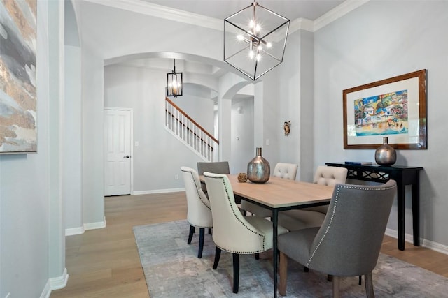 dining space featuring arched walkways, a chandelier, wood finished floors, stairway, and ornamental molding