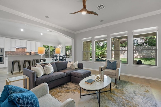living area with baseboards, ceiling fan, crown molding, light wood-style floors, and arched walkways