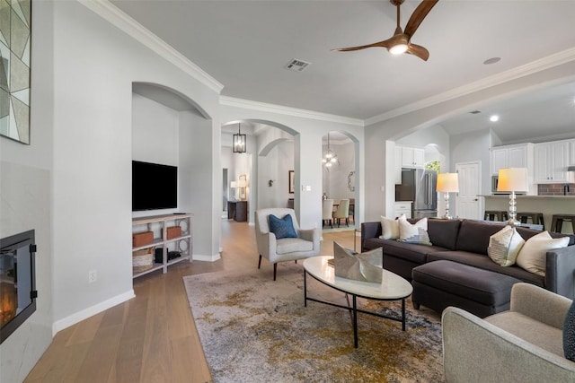 living area featuring arched walkways, crown molding, ceiling fan, wood finished floors, and baseboards