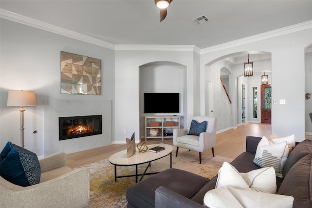 living room featuring ornamental molding, arched walkways, wood finished floors, a premium fireplace, and baseboards