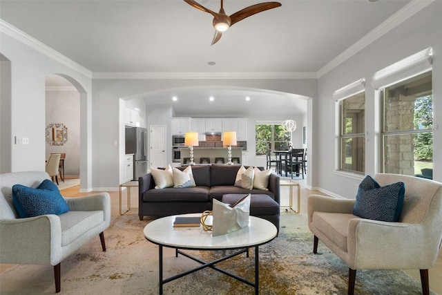 living area with arched walkways, a ceiling fan, crown molding, healthy amount of natural light, and baseboards