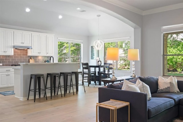 living room featuring light wood-style floors, arched walkways, ornamental molding, and recessed lighting