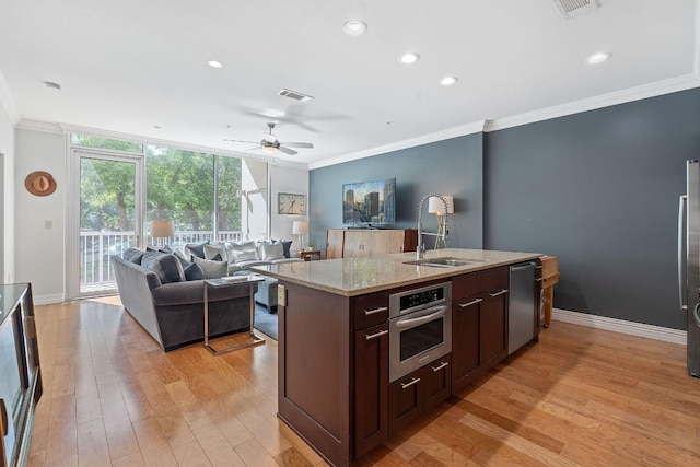 kitchen featuring a sink, appliances with stainless steel finishes, ornamental molding, a center island with sink, and light wood finished floors