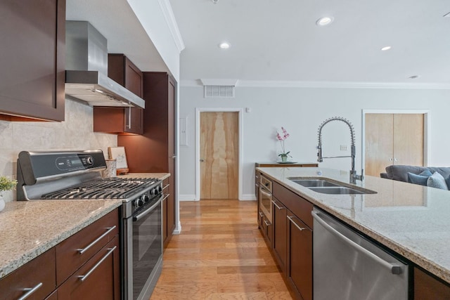 kitchen featuring stainless steel appliances, wall chimney exhaust hood, a sink, ornamental molding, and light stone countertops