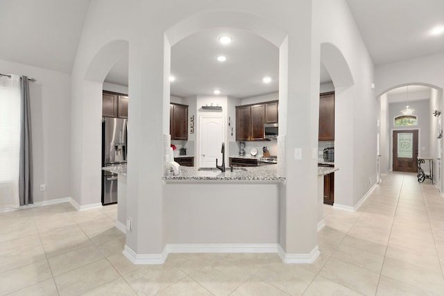 kitchen featuring appliances with stainless steel finishes, light tile patterned floors, dark brown cabinetry, light stone countertops, and a sink