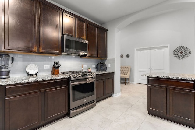 1012 Swan Flower St, Leander, TX 78641 - kitchen featuring appliances with stainless steel finishes, decorative backsplash, light stone counters, dark brown cabinets, and arched walkways