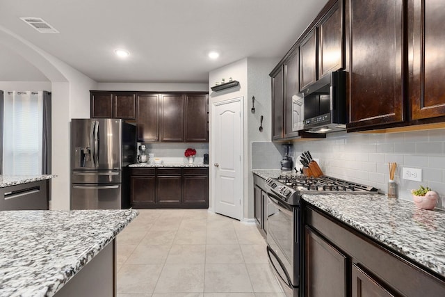 1012 Swan Flower St, Leander, TX 78641 - kitchen featuring appliances with stainless steel finishes, backsplash, arched walkways, dark brown cabinets, and light stone counters