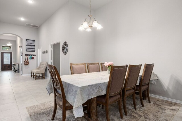 dining area with arched walkways, a chandelier, a high ceiling, light tile patterned floors, and baseboards