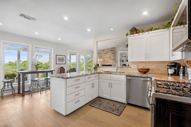 8900 Rockcrest Dr, Austin, TX 78759 - kitchen featuring stainless steel appliances, a sink, a peninsula, backsplash, and light wood finished floors