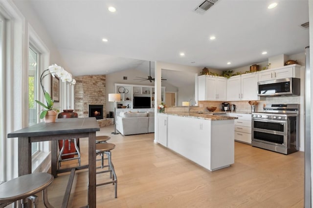 8900 Rockcrest Dr, Austin, TX 78759 - kitchen featuring appliances with stainless steel finishes, white cabinets, backsplash, a ceiling fan, and a stone fireplace