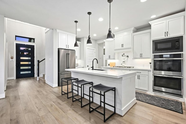 16708 Rakesh Way, Manor, TX 78653 - kitchen with stainless steel appliances, a sink, light countertops, a kitchen bar, and light wood-style flooring