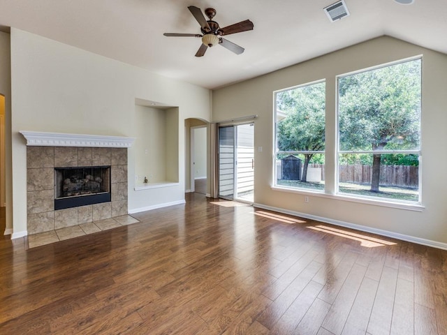 unfurnished living room with wood finished floors, a ceiling fan, a tile fireplace, arched walkways, and baseboards