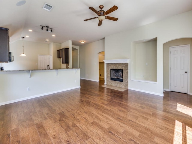 unfurnished living room with arched walkways, a ceiling fan, wood finished floors, a tiled fireplace, and baseboards