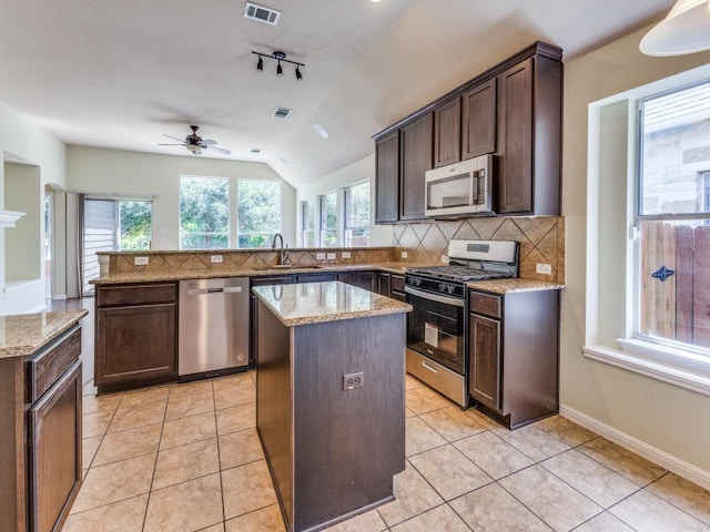 kitchen featuring stainless steel appliances, a kitchen island, a peninsula, a ceiling fan, and decorative backsplash
