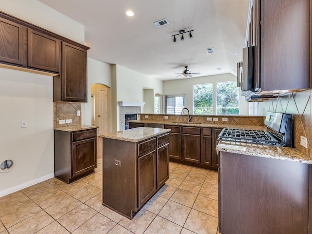kitchen with gas range, a sink, decorative backsplash, ceiling fan, and a tiled fireplace