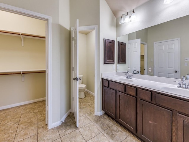 bathroom with toilet, tile patterned flooring, double vanity, and baseboards