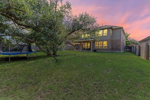 1116 Brenham Ln, Leander, TX 78641 - back of house at dusk featuring a trampoline, a fenced backyard, and brick siding