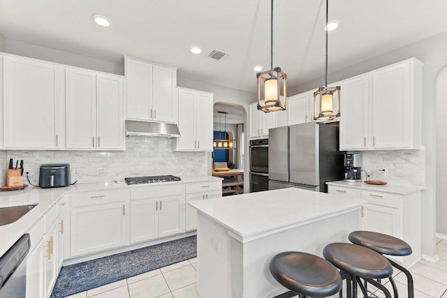 1116 Brenham Ln, Leander, TX 78641 - kitchen featuring under cabinet range hood, stainless steel appliances, arched walkways, backsplash, and light tile patterned floors