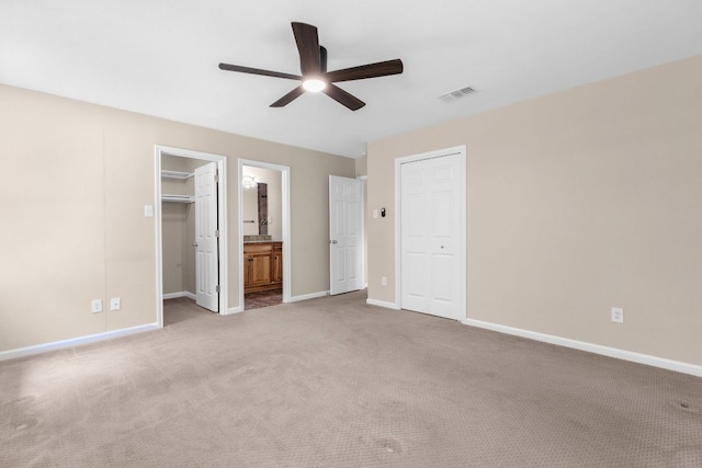 unfurnished bedroom with baseboards, carpet floors, a closet, ensuite bathroom, and ceiling fan