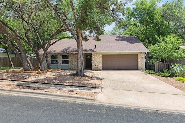 mid-century home with an attached garage, fence, concrete driveway, a shingled roof, and stone siding