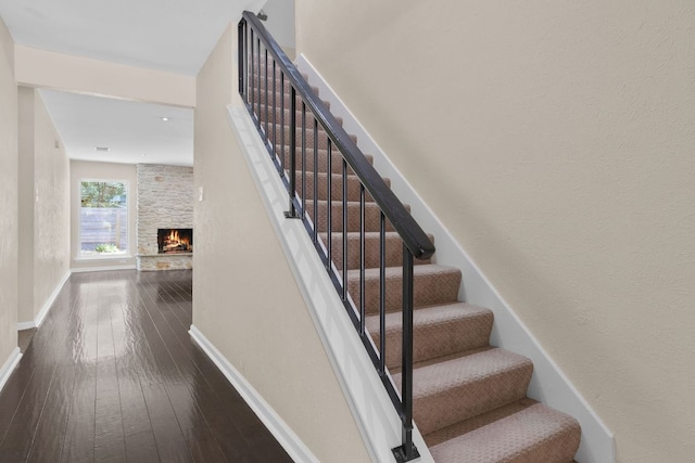 stairway with wood-type flooring, a large fireplace, and baseboards