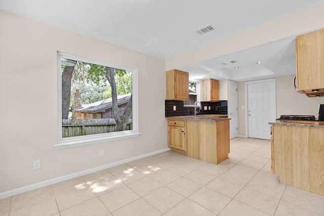 kitchen featuring tasteful backsplash, light tile patterned floors, a tray ceiling, and baseboards