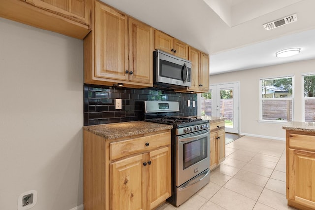kitchen featuring stainless steel appliances, baseboards, backsplash, light tile patterned floors, and stone countertops