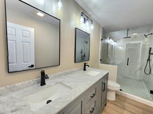 bathroom featuring a marble finish shower, wood finished floors, toilet, and double vanity